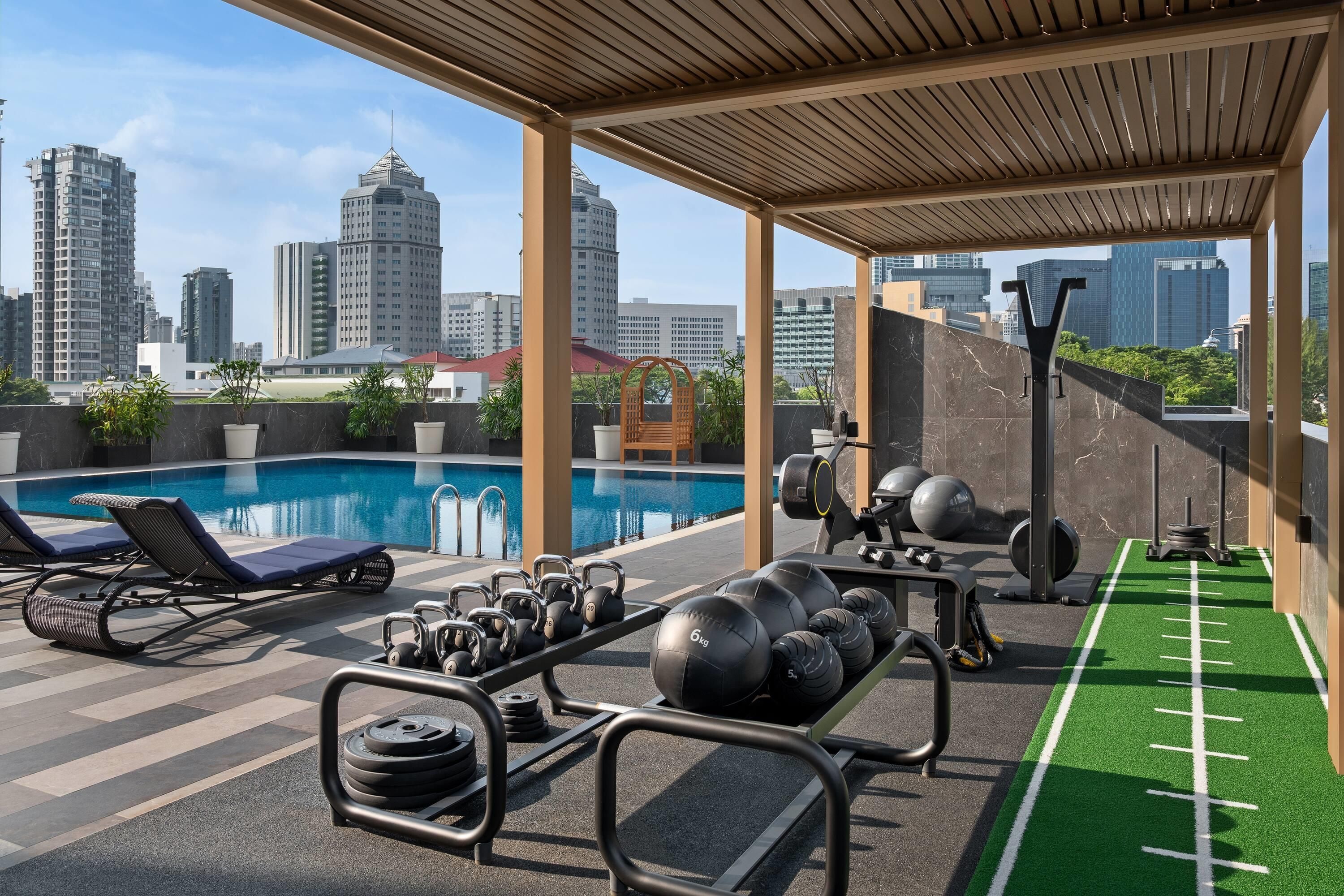 A rooftop gym with exercise equipment, a swimming pool, and city views.
