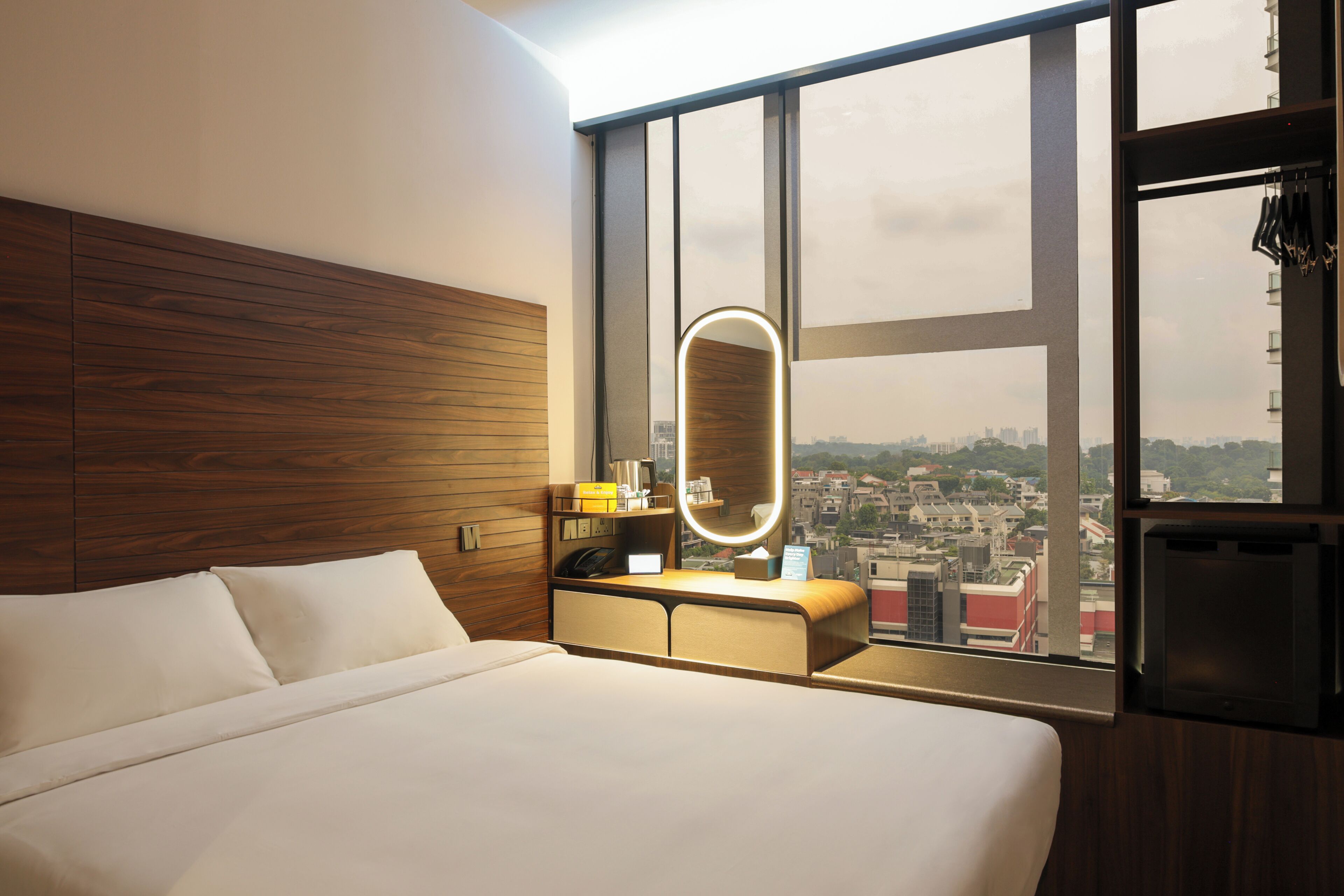 Une chambre d’hôtel avec un grand lit, une table de chevet avec un miroir et une vue sur la ville grâce à de grandes fenêtres.
