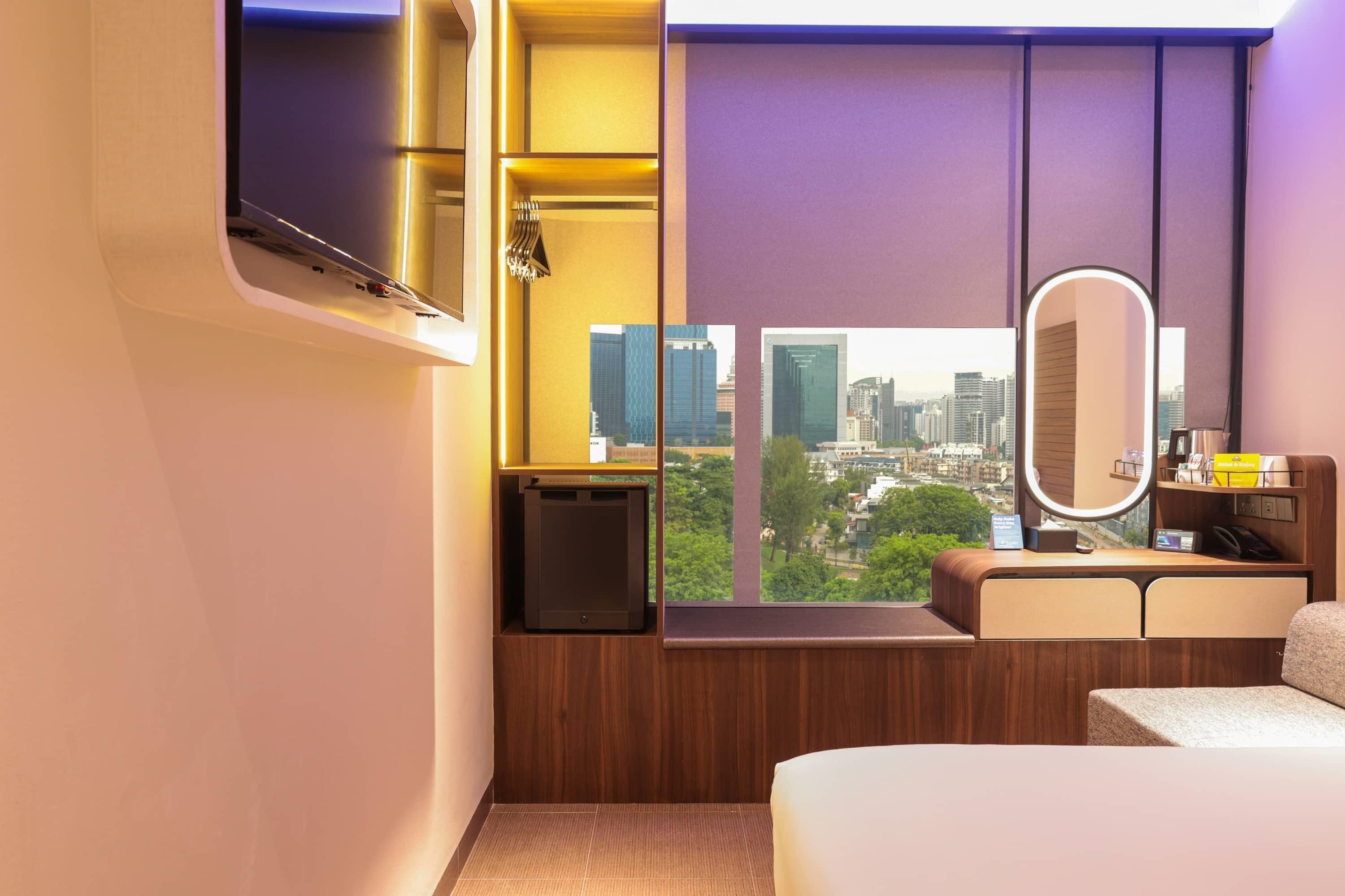 A modern hotel room with a city view, a built-in TV, a bedside table, and a mirror.