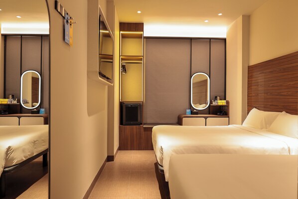 Una habitación de hotel con dos camas, un televisor, un espejo y un cabecero de madera.