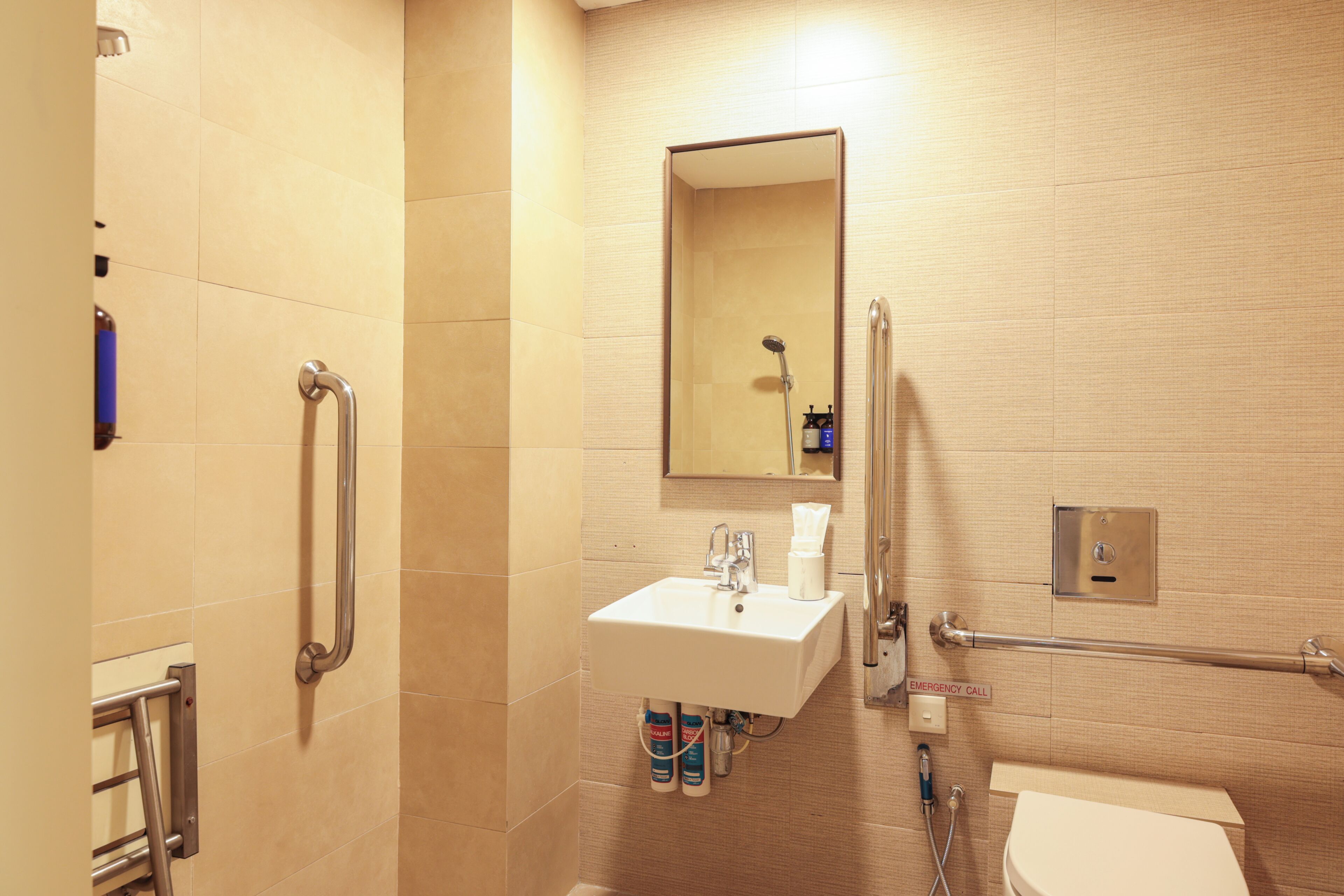 A bathroom with a sink, mirror, handrails, and an emergency call button.