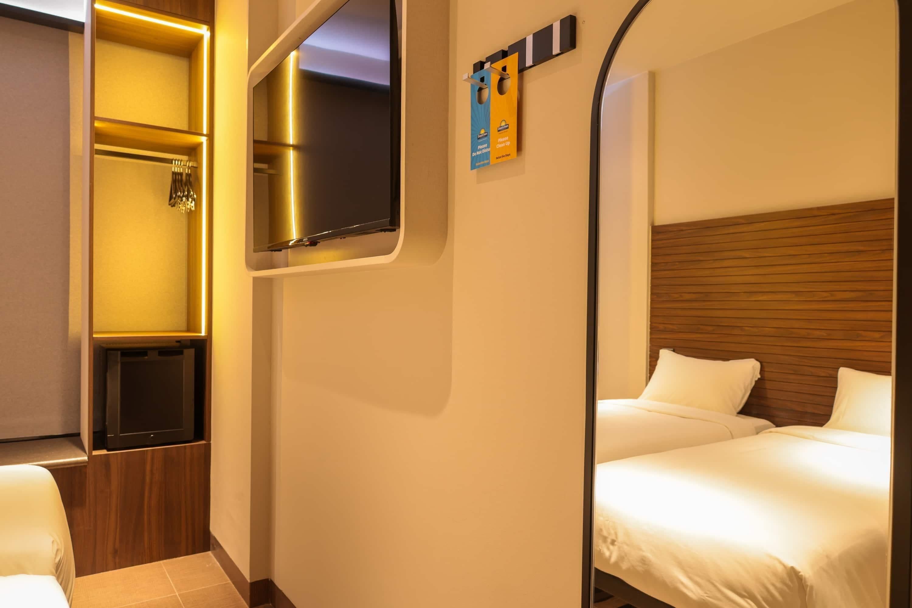 A hotel room with a bed, a mirror, a television, and a shower area.
