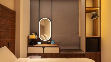 A hotel room with a bed, a bedside table with a lamp, a mirror, and a built-in TV.