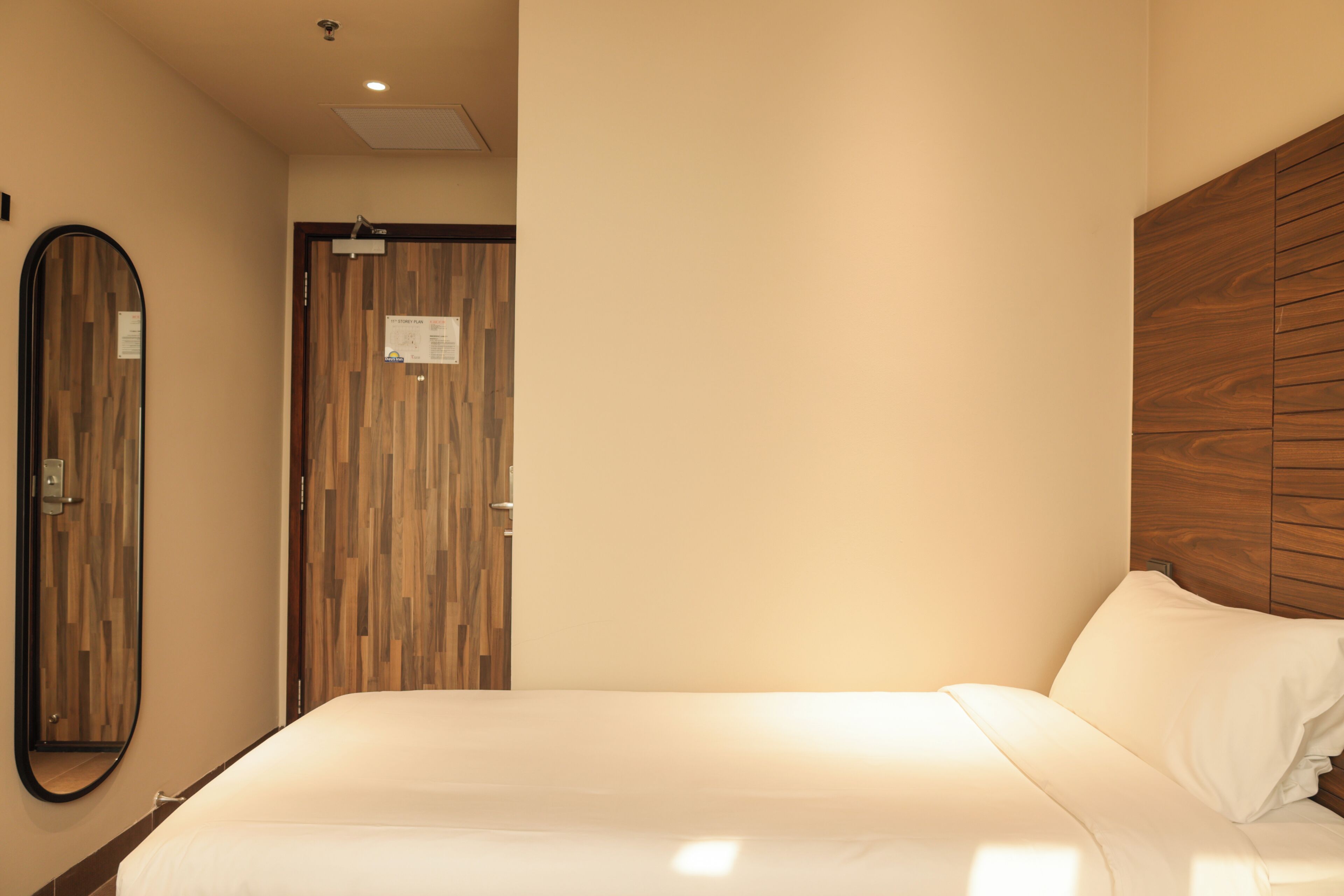 Habitación de hotel con cama, cabecera de madera, espejo y puerta con diseño de panel de madera.
