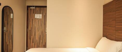 Habitación de hotel con cama, cabecera de madera, espejo y puerta con diseño de panel de madera.