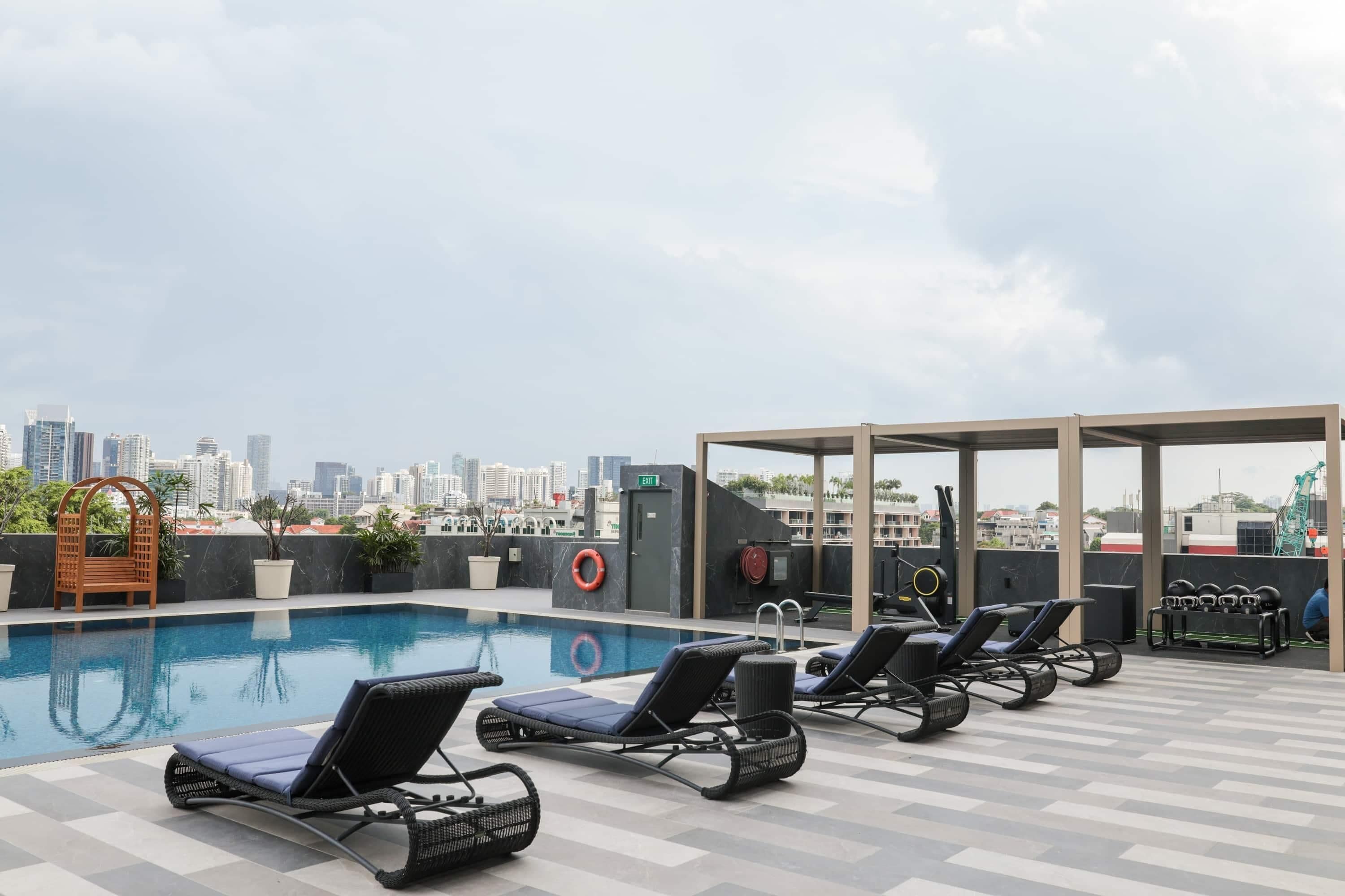 A rooftop pool with lounge chairs, a view of the city skyline, and a covered seating area.