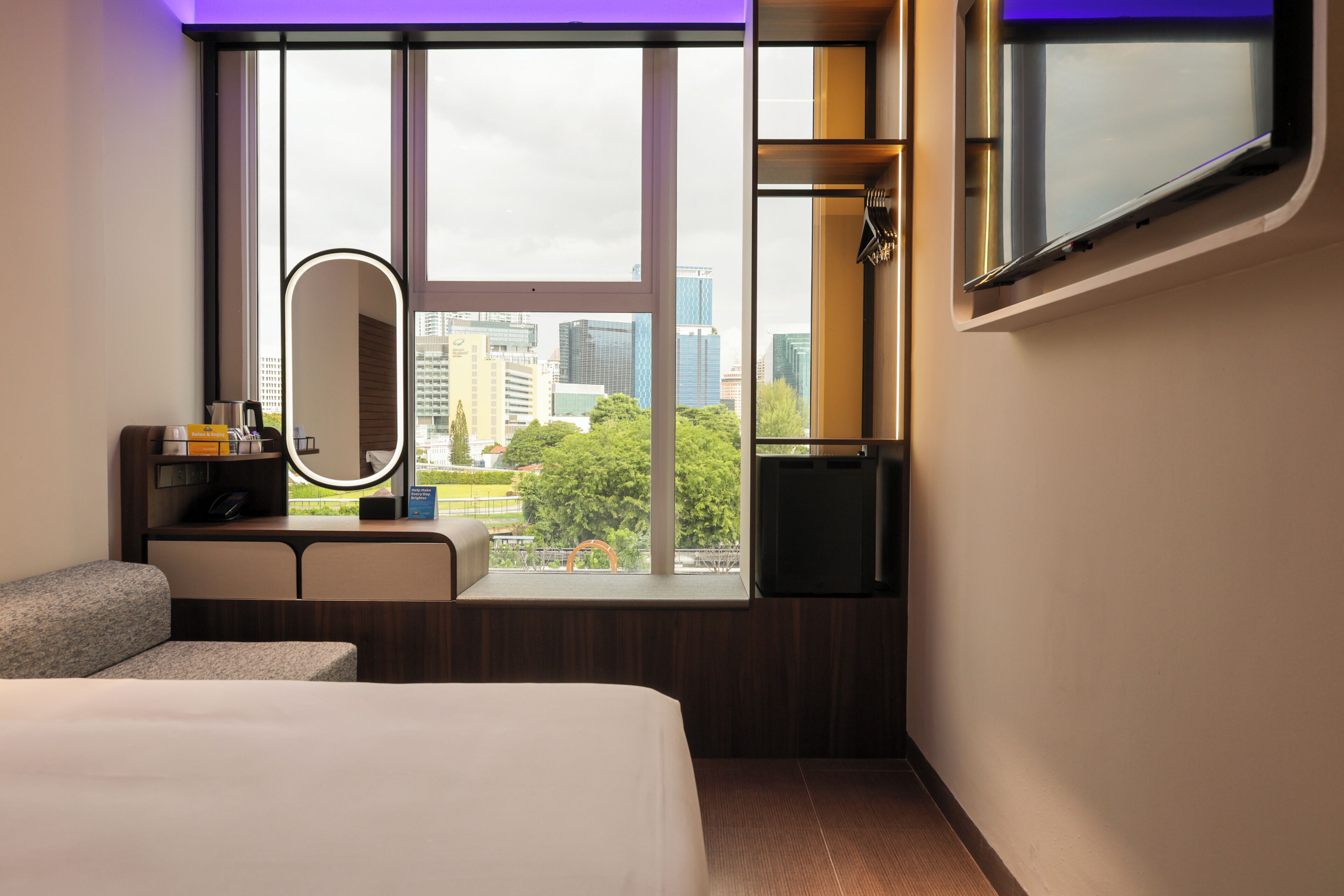 Habitación de hotel con cama, tocador con espejo, televisión y ventana con vista a la ciudad.