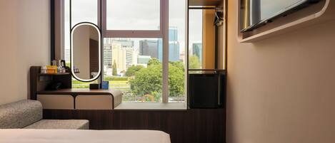 Habitación de hotel con cama, tocador con espejo, televisión y ventana con vista a la ciudad.