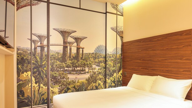 Habitación de hotel con una cama grande, cabecera de madera y un mural de un jardín con estructuras singulares.