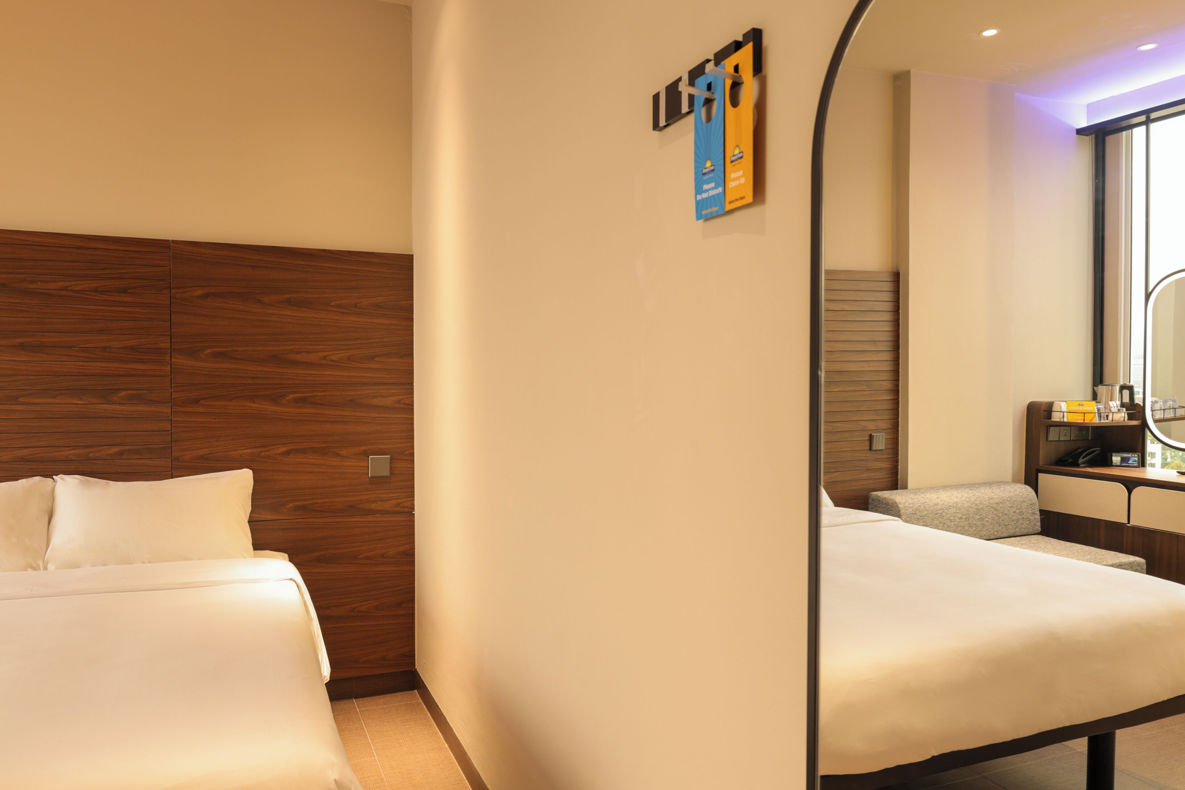 Una habitación de hotel con cabecera de madera, cama con ropa blanca, escritorio con silla y espejo.