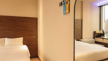 Ett hotellrum med en sänggavel i trä, en säng med vita sängkläder, ett skrivbord med en stol och en spegel.