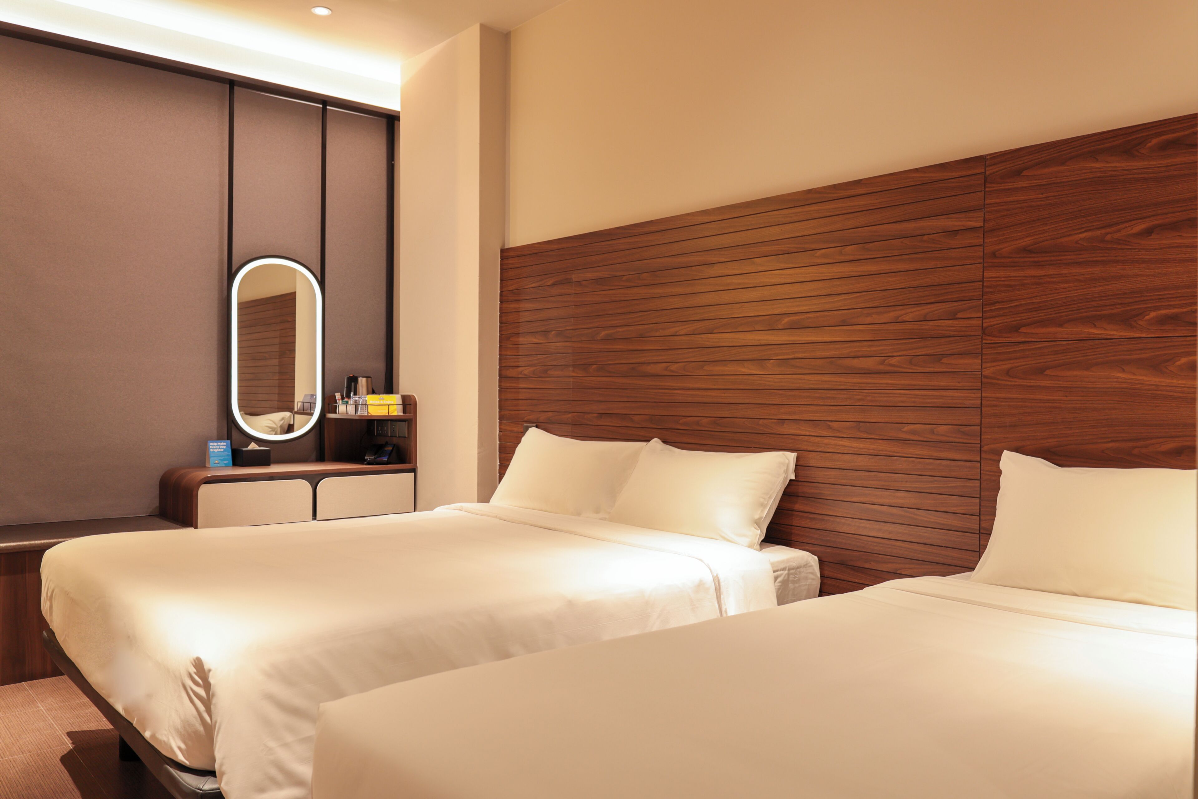A hotel room with two beds, a wooden headboard, a bedside table, and a mirror.