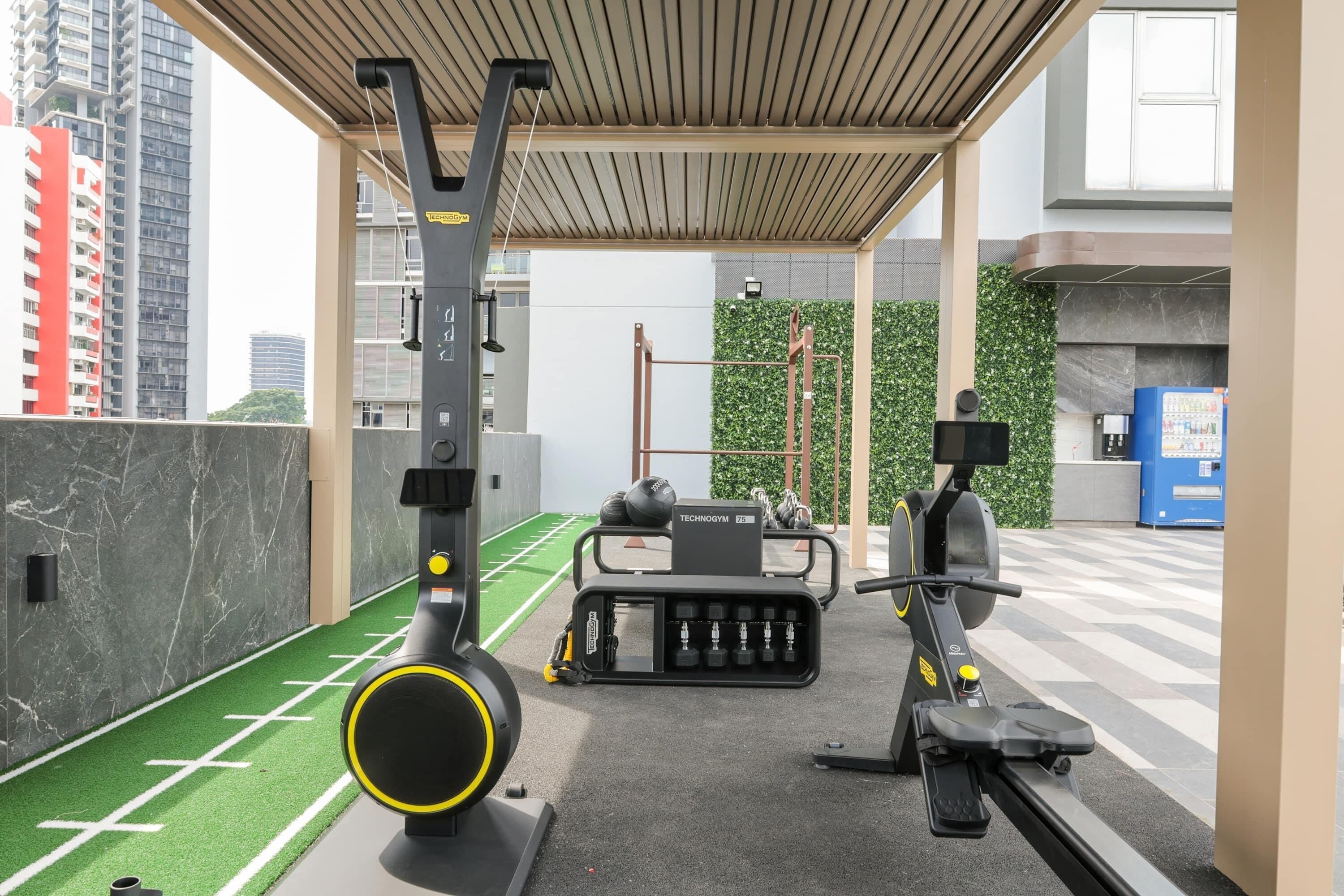 A gym with exercise equipment, a green artificial turf area, and a cityscape view.