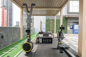 Un gimnasio con equipamiento de ejercicio, una zona de césped artificial verde y vistas a la ciudad.