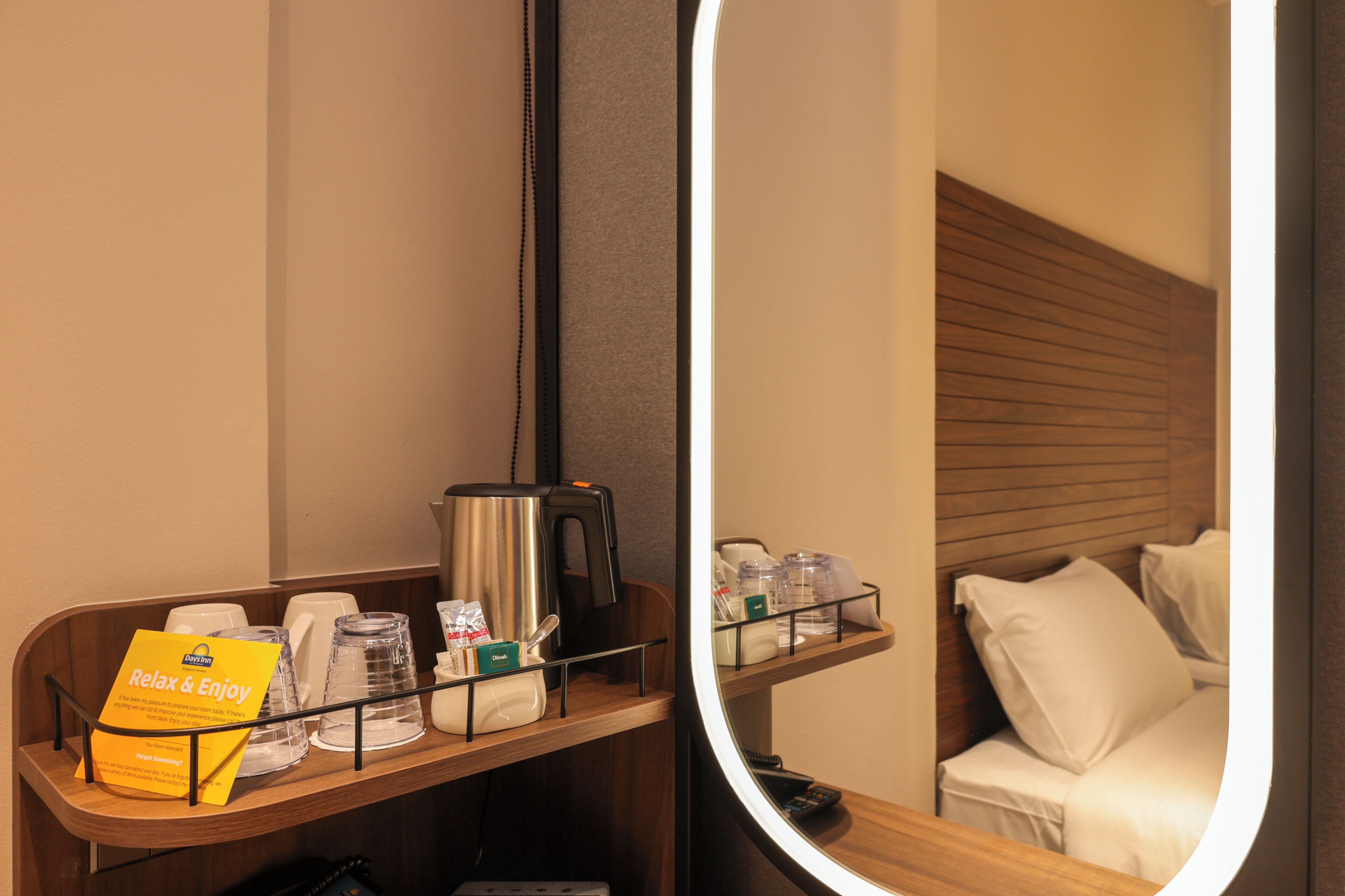 A hotel room with a wooden headboard, a bedside table with a coffee maker, a tray with amenities, and a mirror reflecting the room.