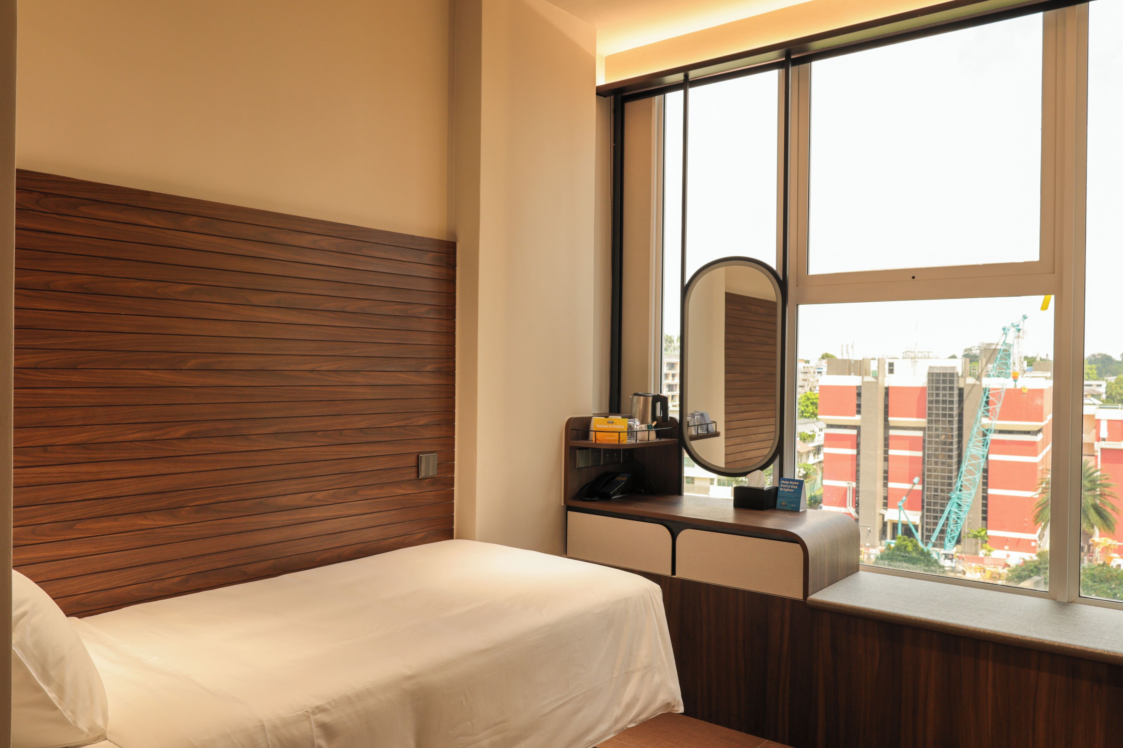 Habitación de hotel con cabecera de madera, cama, escritorio con espejo y ventana con vista a la ciudad.