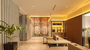 Un interior moderno con sofá, una mesita, una planta en maceta y un revestimiento decorativo con líneas verticales.