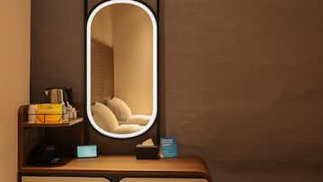 Habitación de hotel con mesita de noche, espejo, lámpara de noche, teléfono, caja de pañuelos y un cartel que dice 'Relax & Enjoy'.