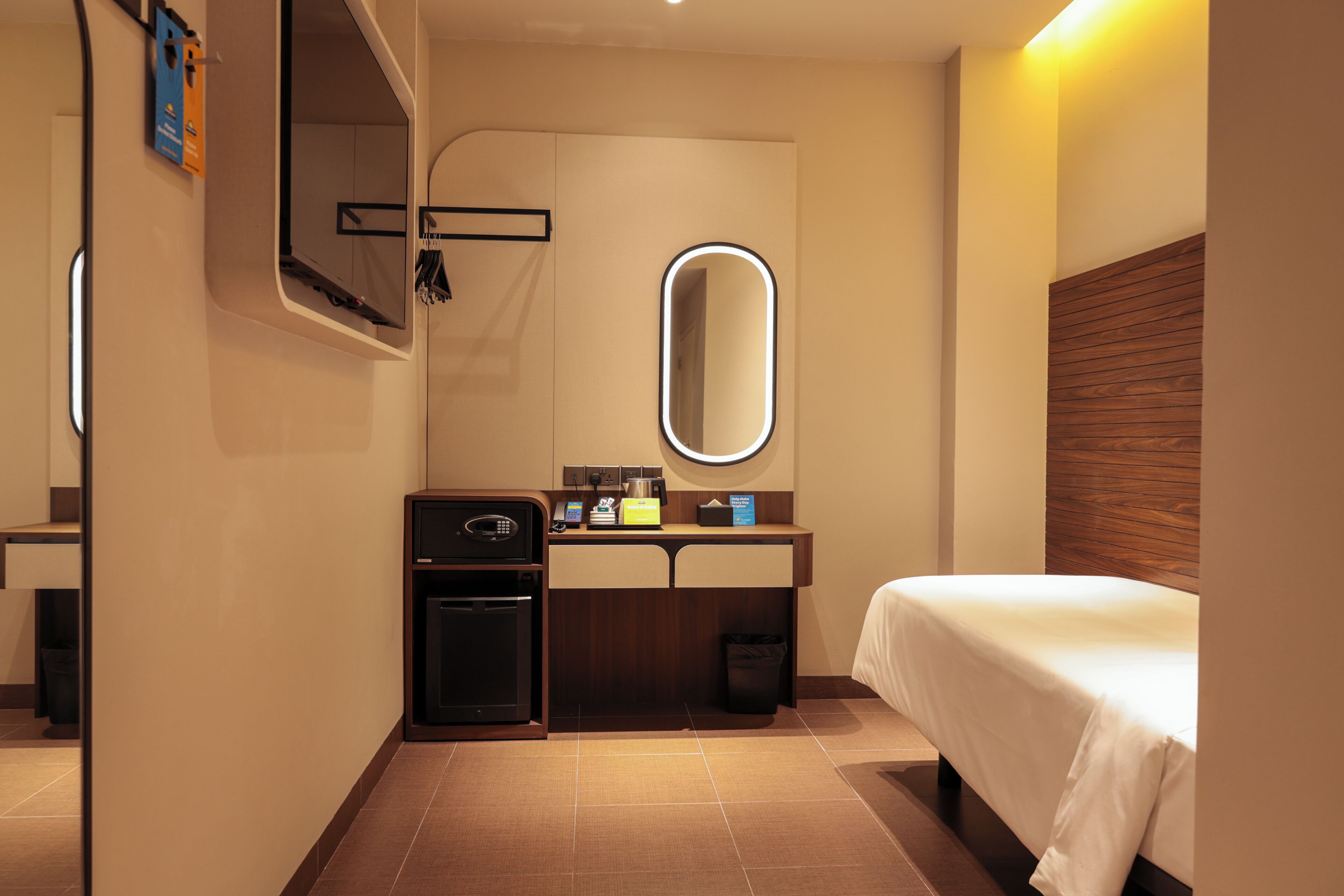 A hotel room with a bed, a mirror, a small desk with a microwave, and a trash bin.
