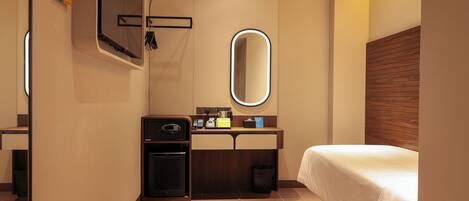 A hotel room with a bed, a mirror, a small desk with a microwave, and a trash bin.
