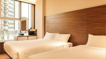 Une chambre d’hôtel avec deux lits, une tête de lit en bois, une grande fenêtre et un miroir rond.