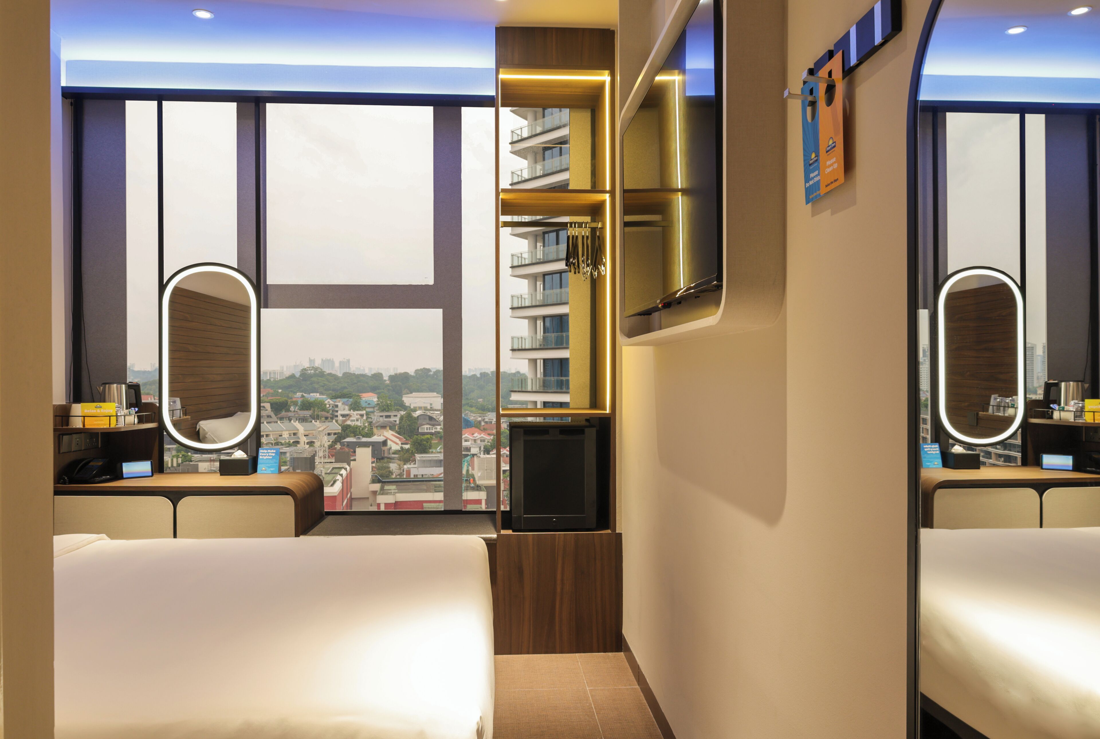 Quarto de hotel com uma cama, televisão, espelho e vista para a cidade.