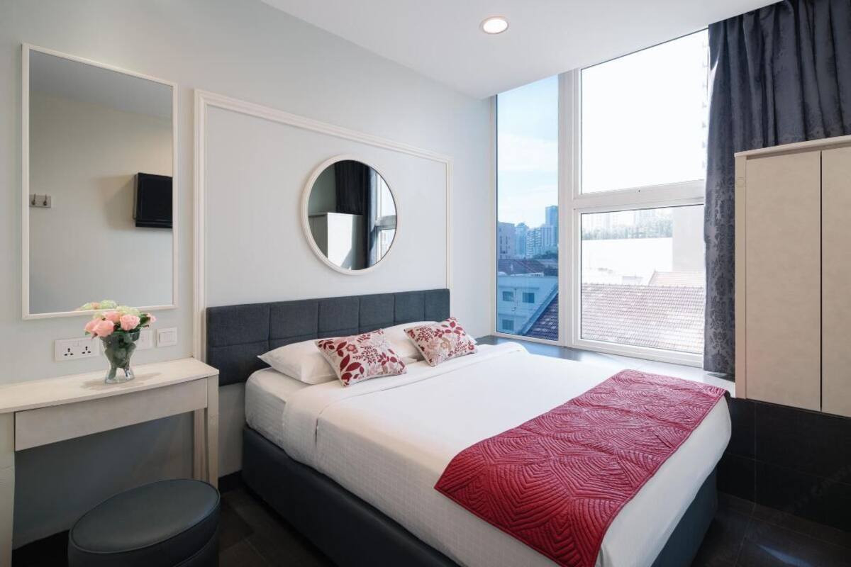 A modern bedroom with a large bed, a round mirror, a vanity with a mirror, and a window with a city view.