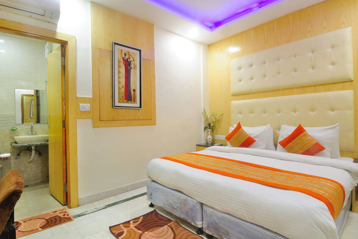 A hotel room with a large bed, a wooden headboard, a framed picture on the wall, and a bathroom visible through an open door.