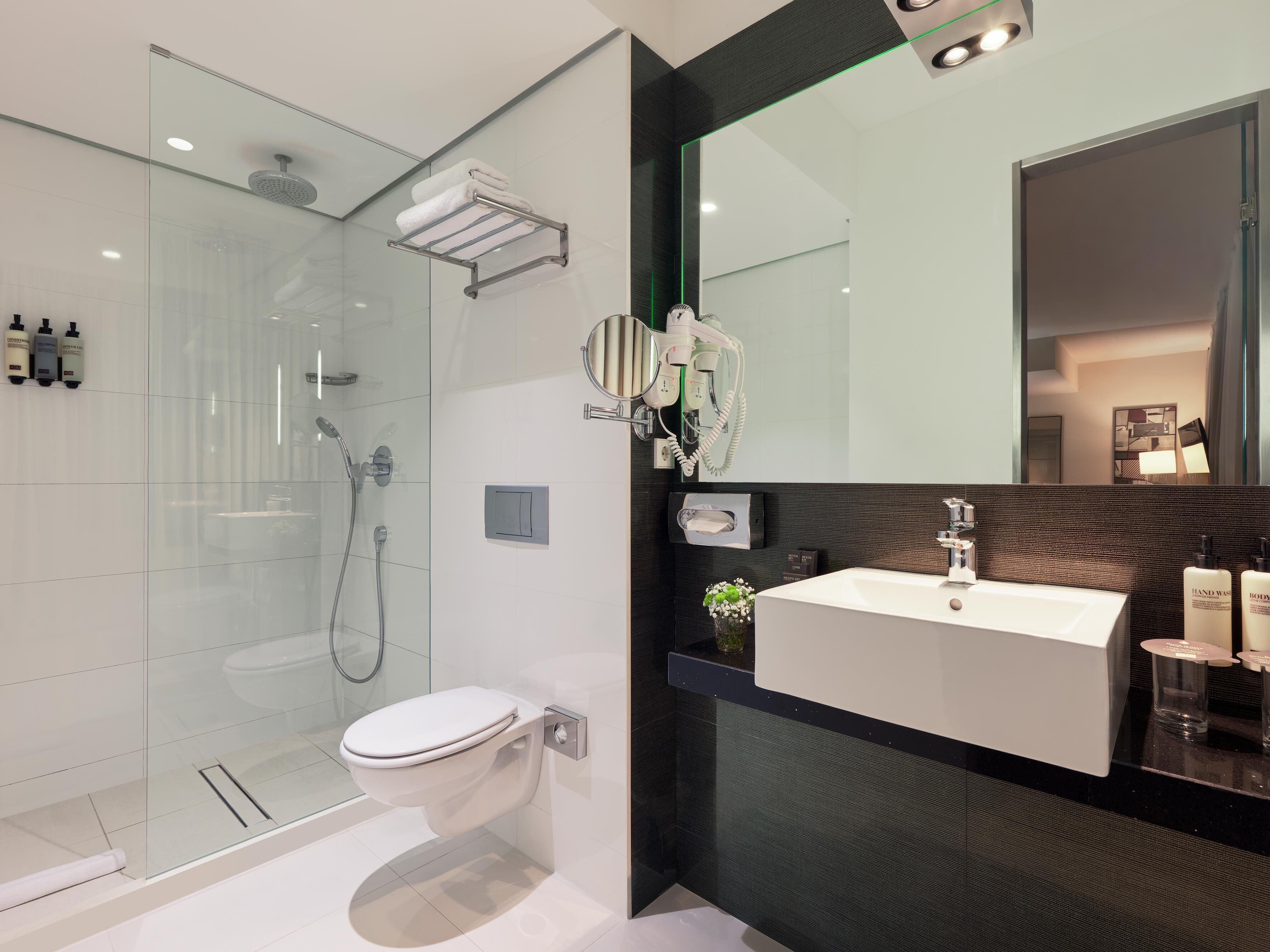 Un baño moderno con cabina de ducha de vidrio, inodoro blanco, tocador con espejo y artículos de aseo.