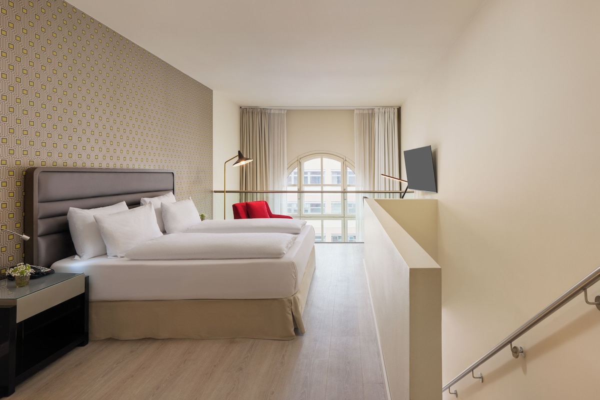 A modern hotel room with a bed, bedside table, lamp, and a TV on the wall.