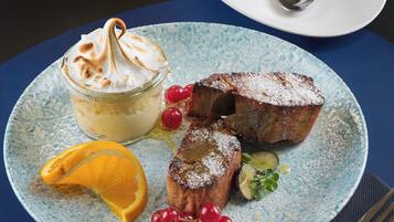 A dessert plate with a meringue, fruit, and powdered sugar, a white cup and saucer, and a spoon on a blue tablecloth.