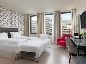 Habitación de hotel con dos camas, una silla roja, un escritorio con cafetera y un televisor.