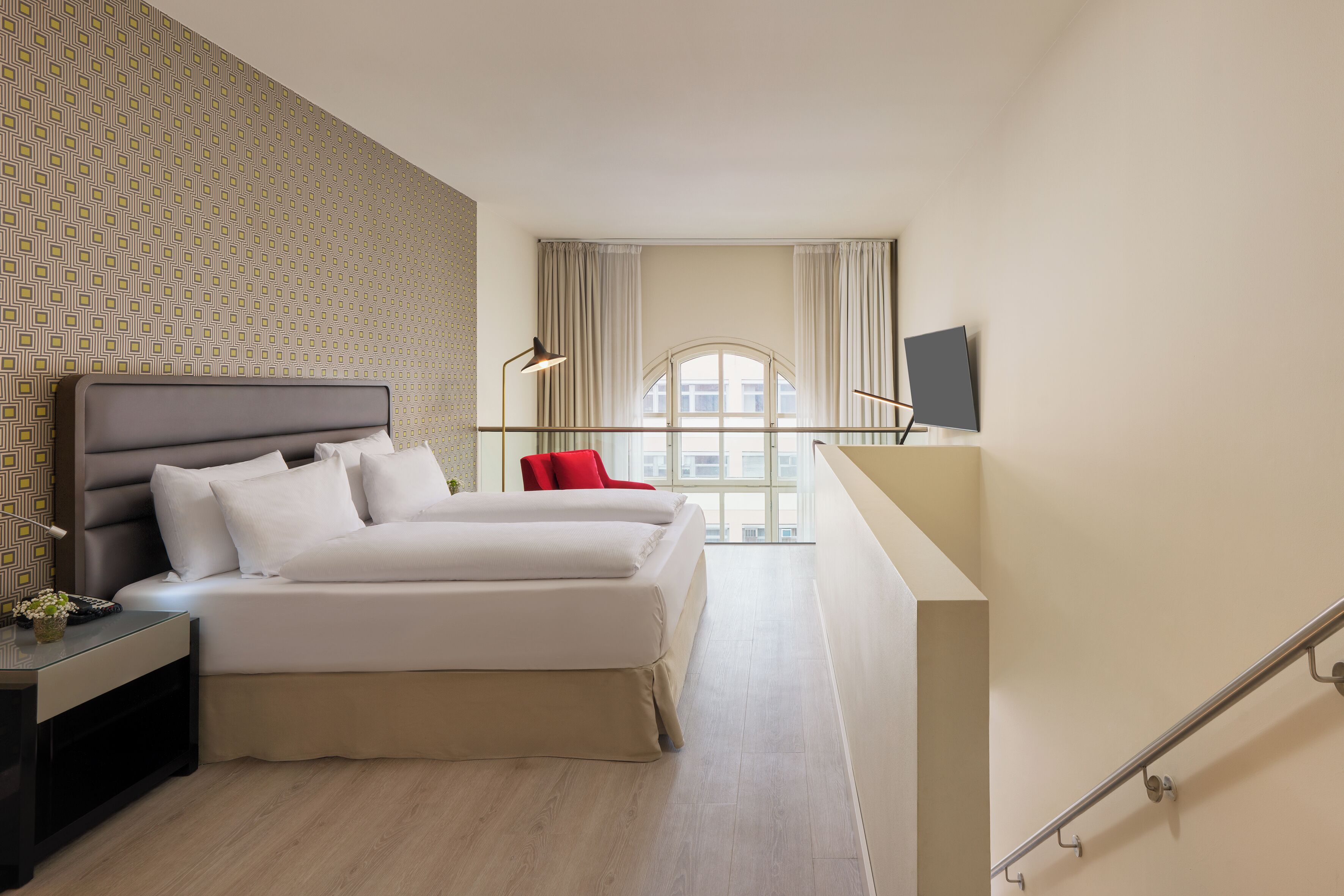 A modern hotel room with a bed, bedside table, lamp, and a TV on the wall.