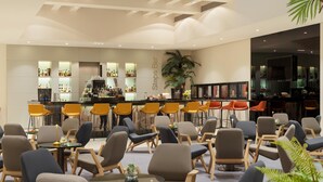 Un moderno vestíbulo de hotel con zona de bar, asientos y una planta grande en maceta.