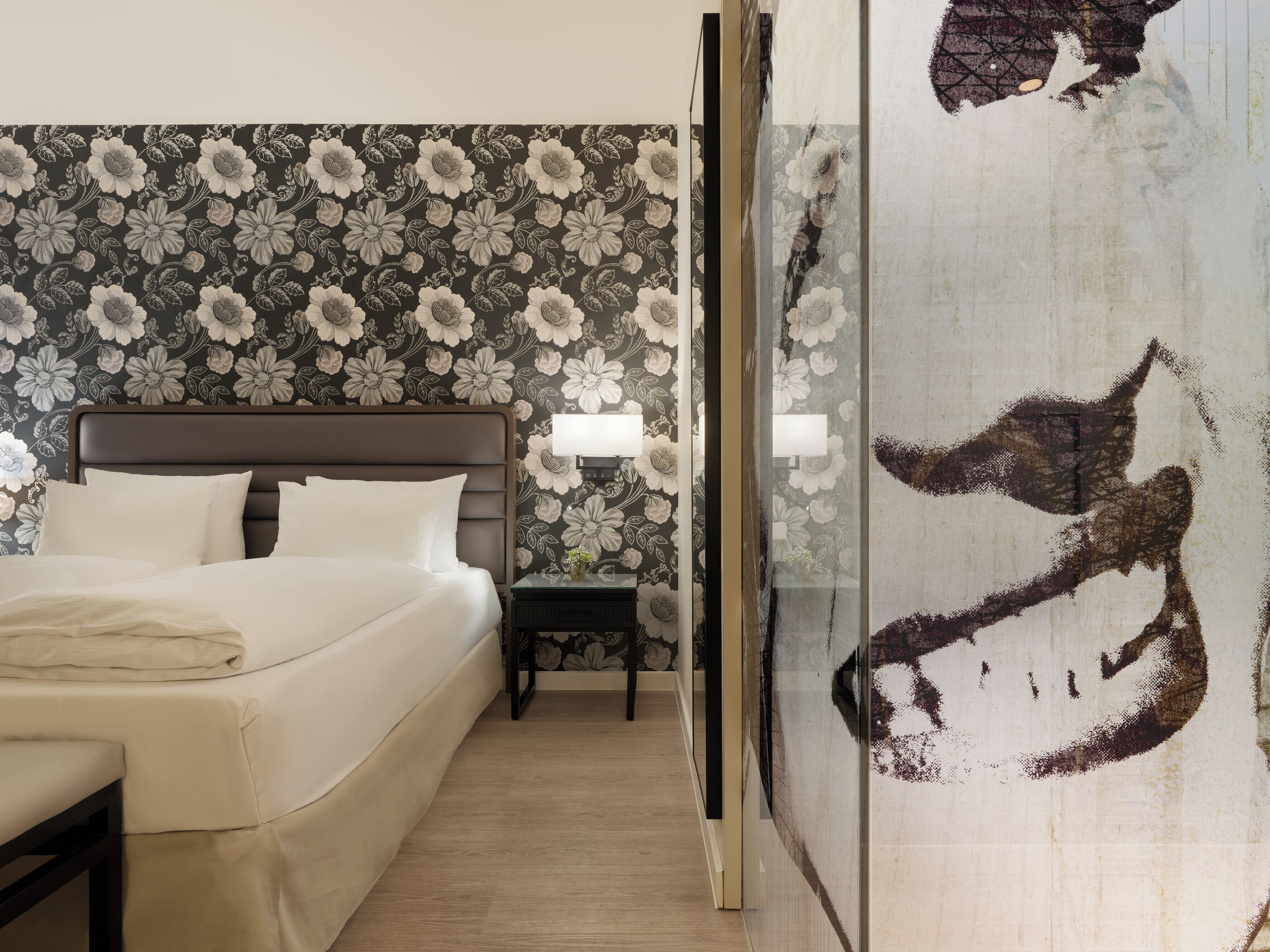 Una habitación de hotel con una cama, mesita de noche y un papel tapiz floral.