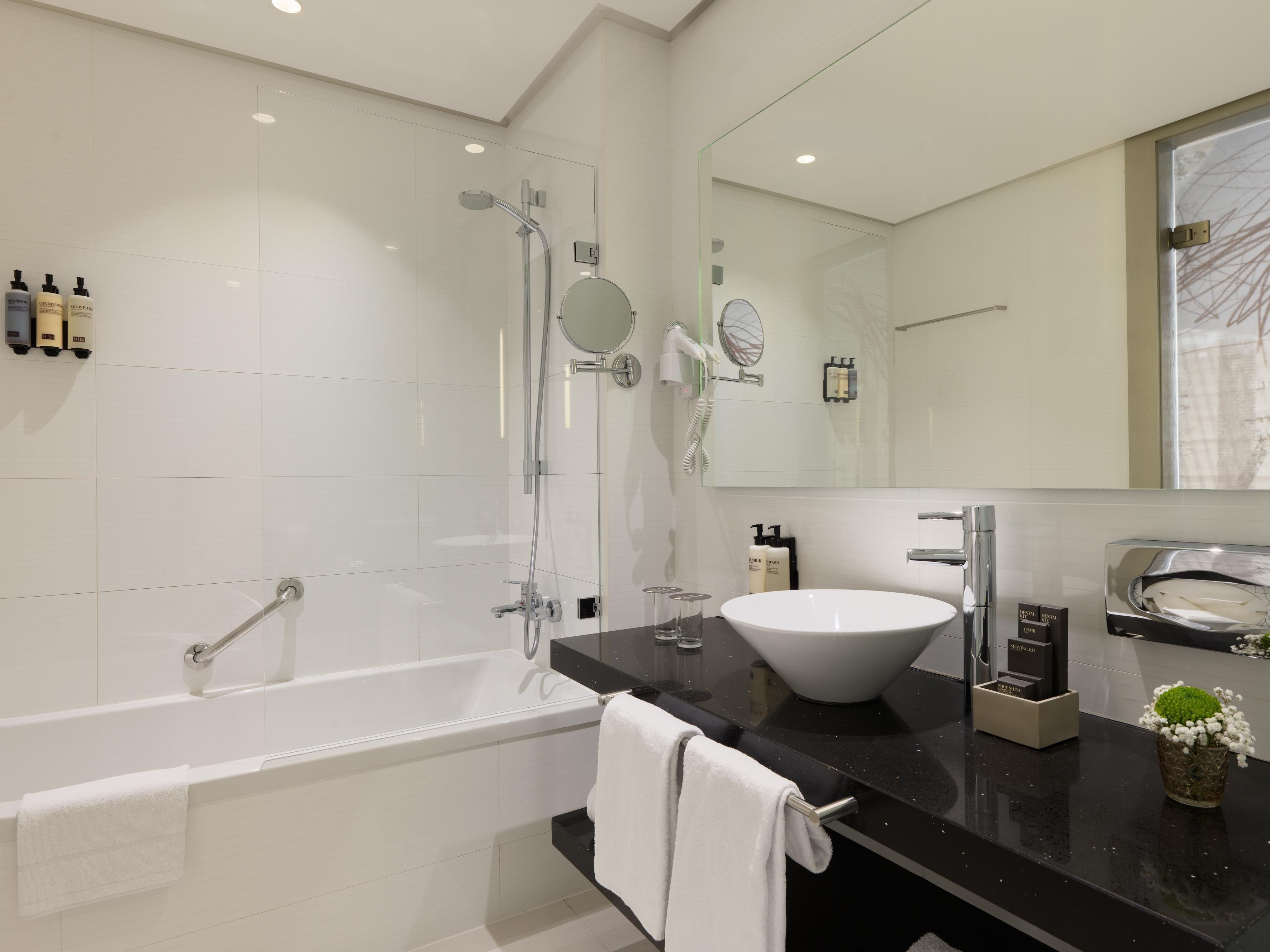 Een moderne badkamer met een badkuip, een grote spiegel, een wastafel en toiletartikelen op het aanrecht.