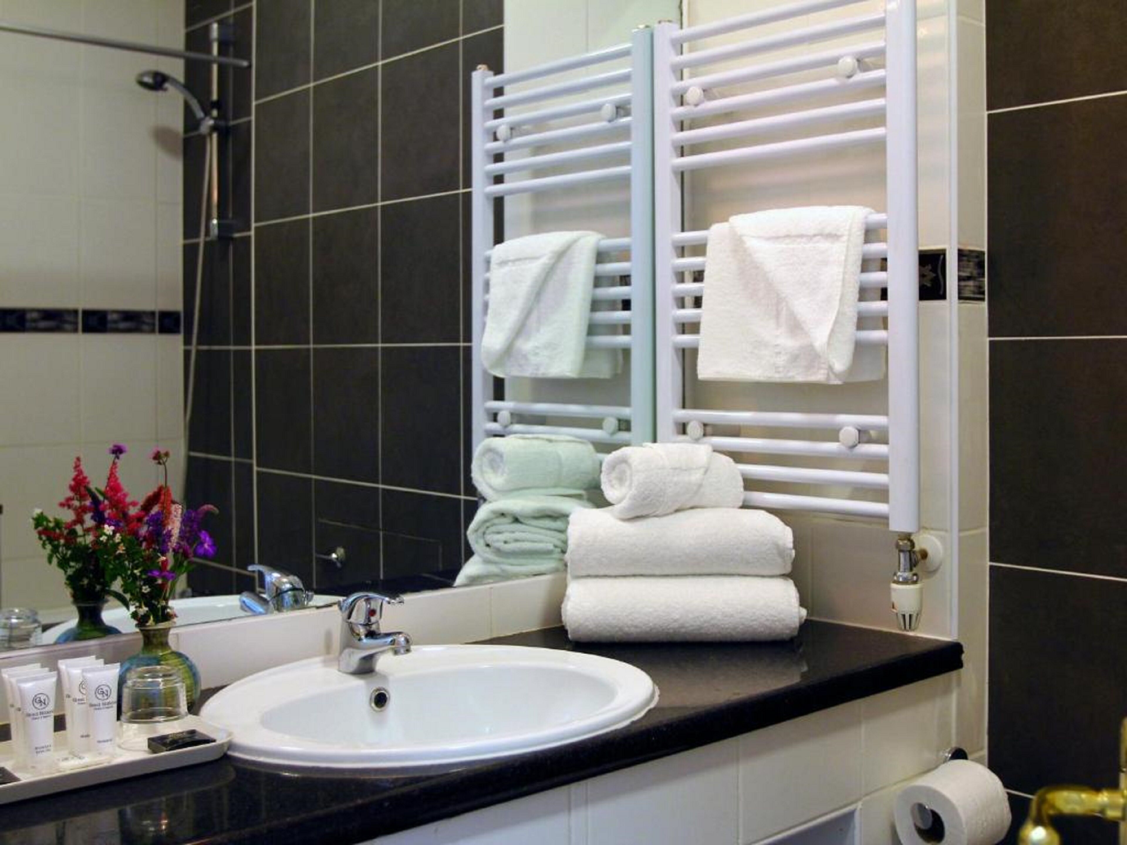 Une salle de bain d’hôtel avec un lavabo blanc, un miroir, un porte-serviettes avec des serviettes pliées et des articles de toilette posés sur le comptoir.