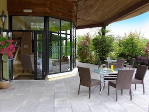 Un patio exterior con puerta de vidrio, sillas de mimbre y una mesa lista para comer.