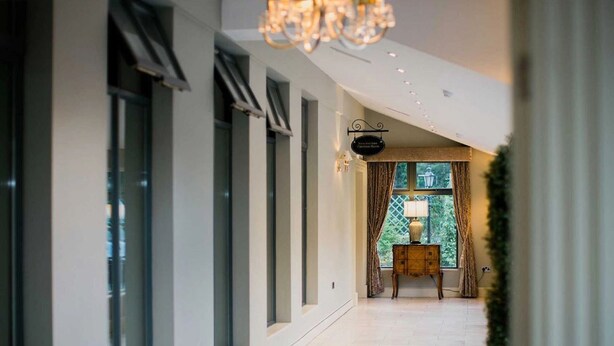 A hallway with large windows, a chandelier, and a small table with a lamp. - Abbeyleix Manor Hotel (Abbeyleix)
