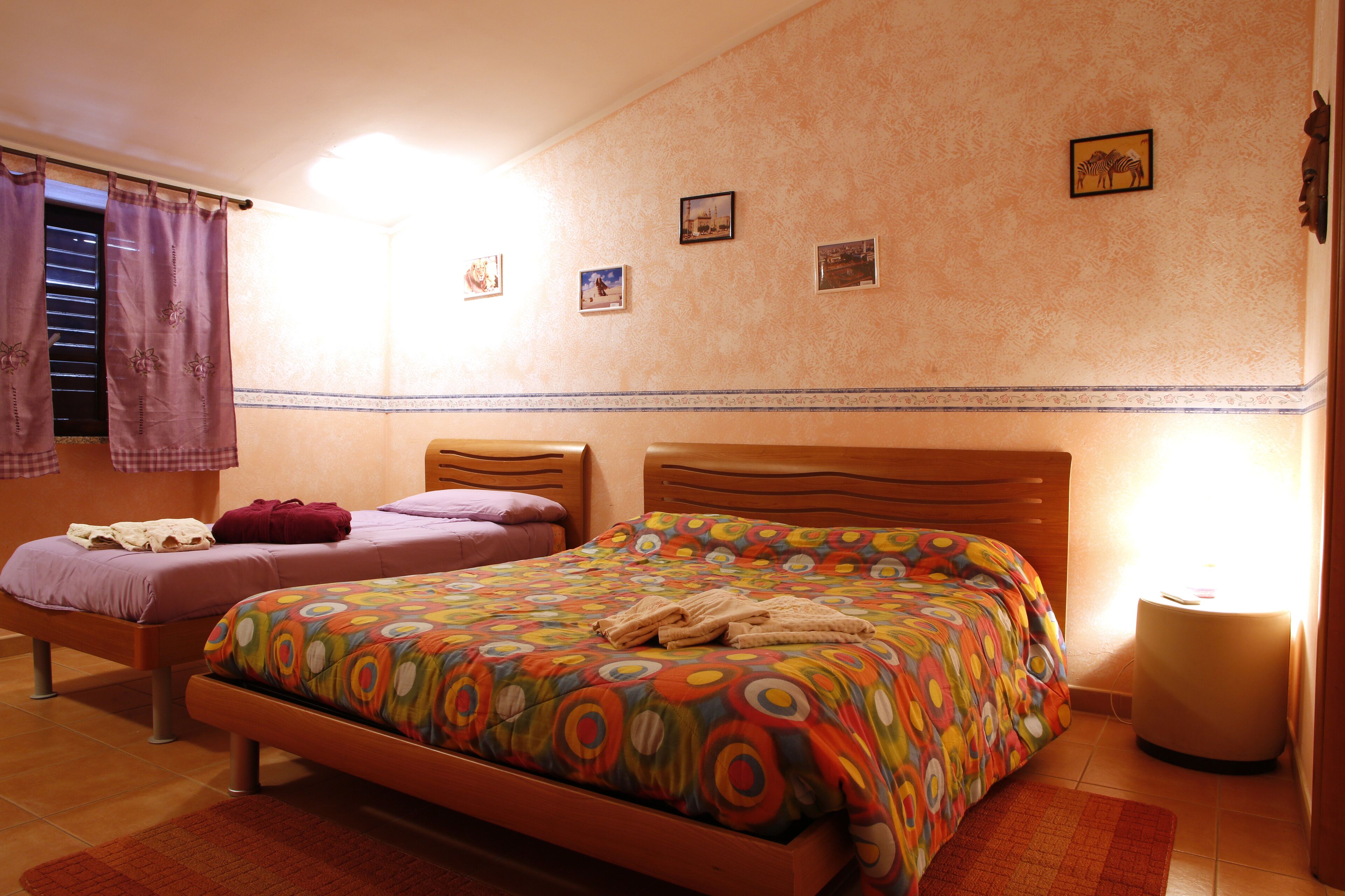 Quarto com duas camas, uma mesa de cabeceira e uma parede com quadros.