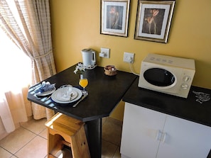 Una cocina compacta con microondas, una pequeña mesa lista para el desayuno y dos cuadros en la pared.