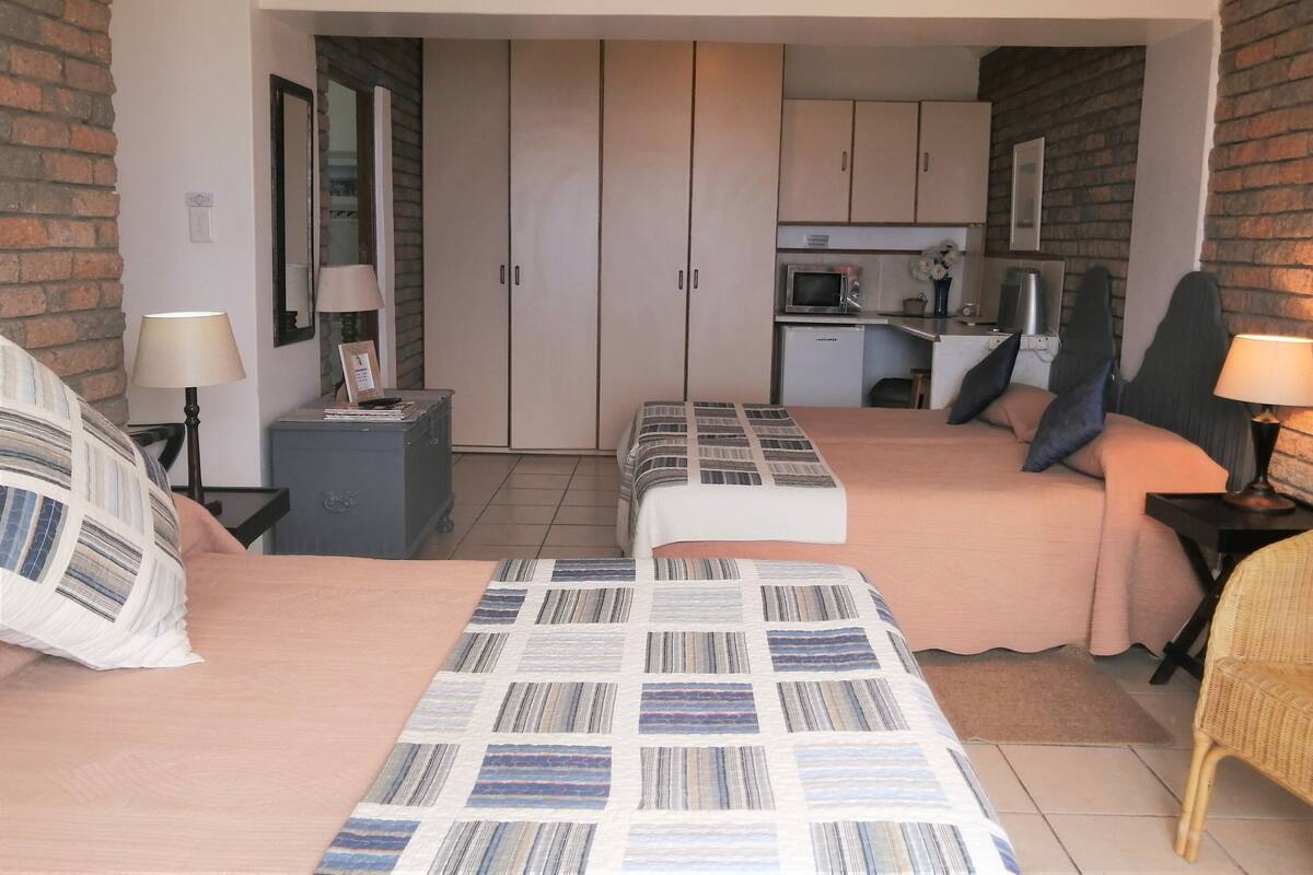Habitación de hotel con dos camas, una kitchenette pequeña y una pared de ladrillo.