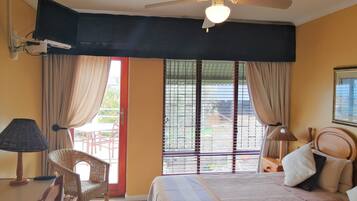 A hotel room with a bed, a chair, a desk, a ceiling fan, and a window with blinds.