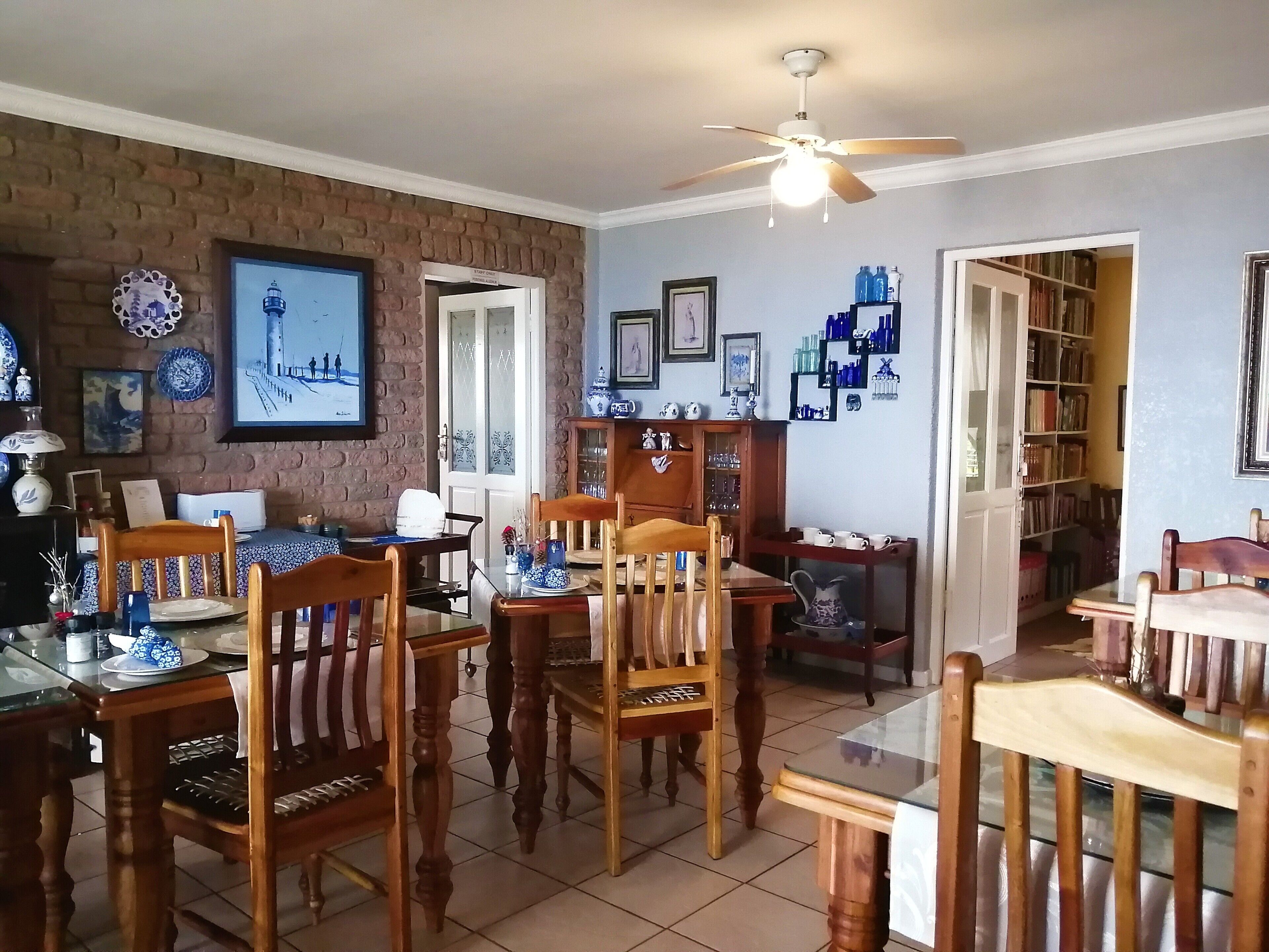 A dining area with wooden chairs and tables, a brick wall, and a ceiling fan.