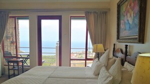 Habitación de hotel con una cama grande, dos mesitas de noche, una silla y vista al mar.