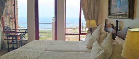 A hotel room with a large bed, two bedside tables, a chair, and a view of the sea.