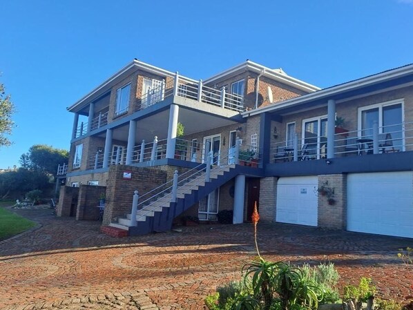 A two-story house with a balcony, a garage, and a brick driveway. - Amzee Bokmakierie Guest House (Mossel Bay)