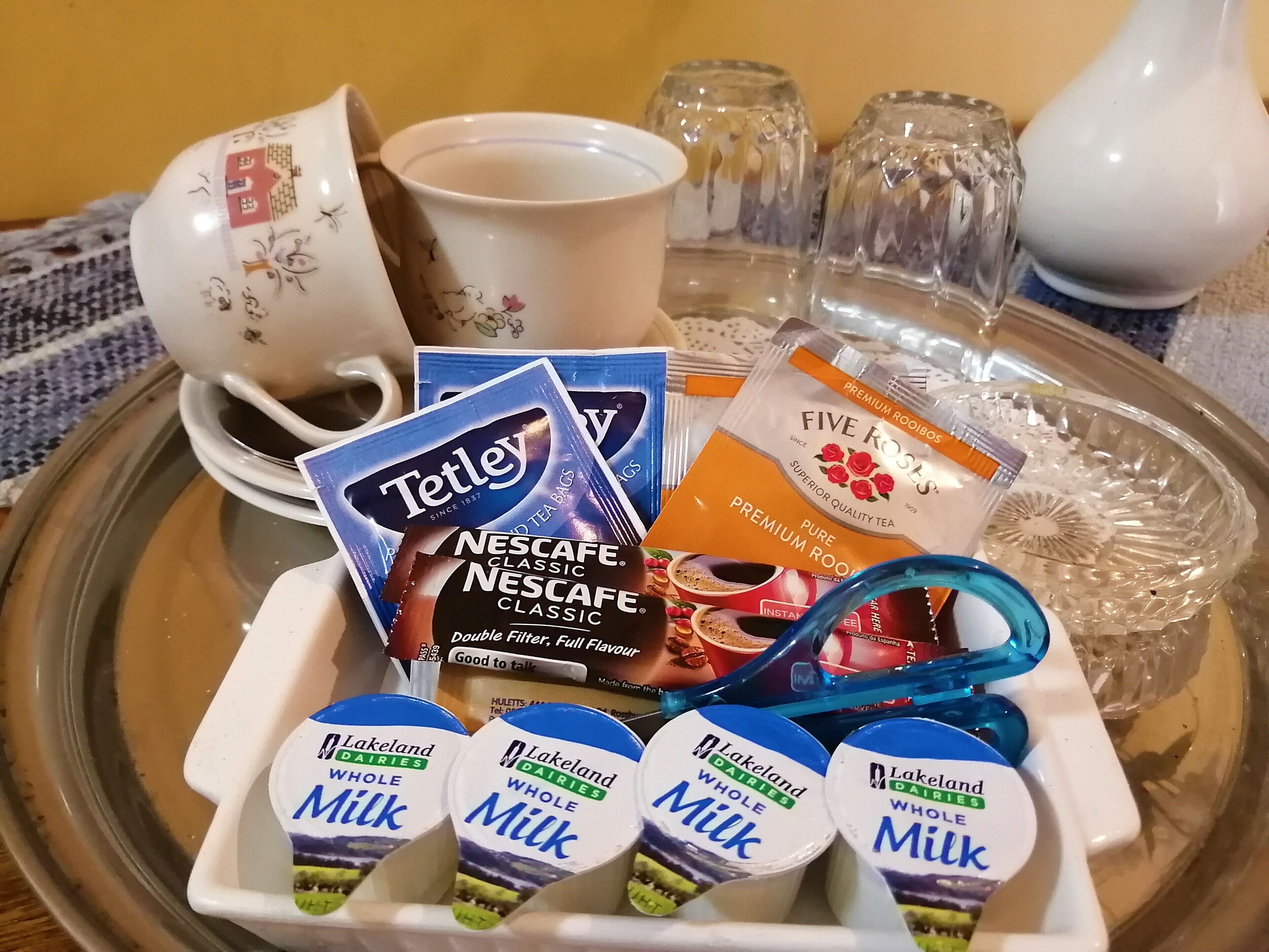 A tray with Tetley tea bags, Nescafe Classic coffee, Lakeland dairies whole milk, and a white cup with floral designs.