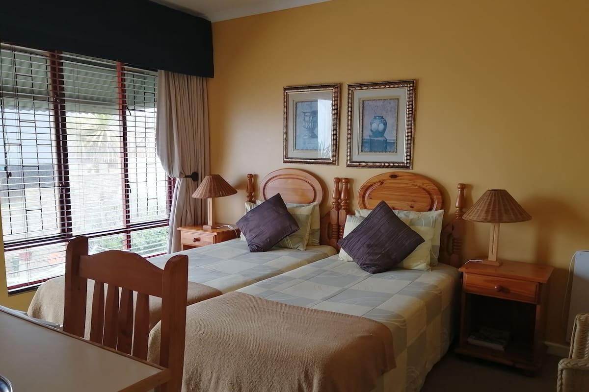 Un lit double avec une tête de lit en bois, deux tables de chevet avec des lampes, une chaise et une fenêtre avec des rideaux.