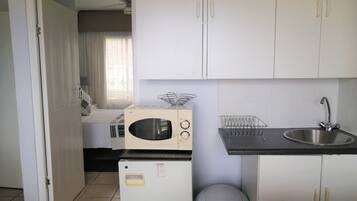 A compact kitchen with white cabinets, a microwave, a small refrigerator, and a sink.